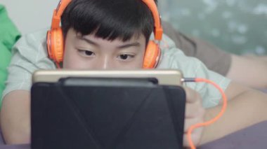 Genç Asyalı mutlu çocuk gülen yüzle tableti kullanıyor..