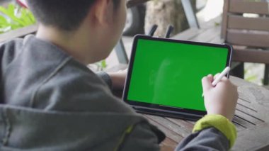 Yeşil ekran renk anahtarı ile tablet bilgisayara bakan çocuk.