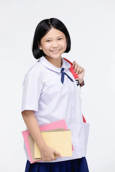 Menina bonito no uniforme do estudante com artigos de papelaria em fundo cinza — Fotografia de Stock