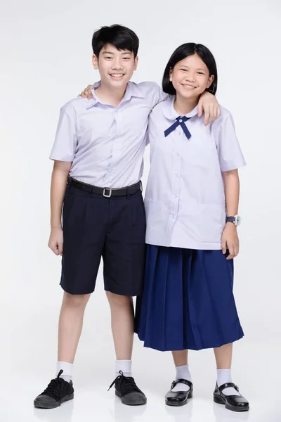Aasijská dívka a kluk ve studentově uniformě na šedém pozadí. — Stock fotografie