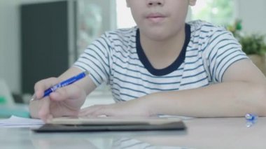 Asyalı çocuk cevapları bulmak için bir tablet kullanarak ev ödevi yapıyor evde bir sandalyeye oturur.