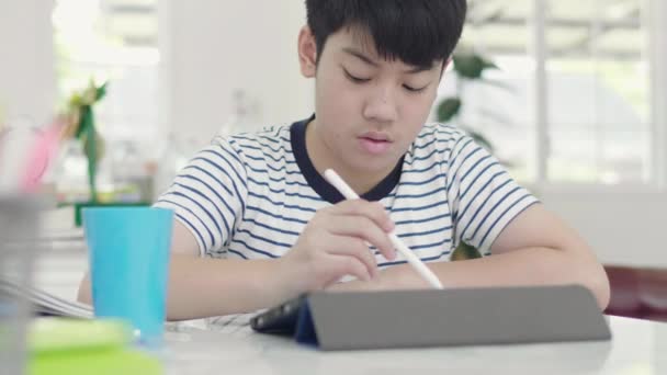 アジアの少年は答えを見つけるためにタブレットを使用して宿題のために自宅の椅子に座ります — ストック動画