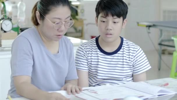母は息子が家で宿題をするのを手伝っている 美しい母親が教科書を読み 家で一緒に宿題をしながら息子と話す — ストック動画