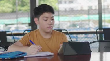 Mutlu küçük çocuk tablet bilgisayarla ev ödevi yapıyor. Asyalı çocuk masada oturan ve ödevini yapıyor Okul, çocuklar, eğitim kavramı.