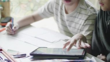 Mutlu küçük çocuk tablet bilgisayar ile ödevini yapıyor. Evde ki masada oturan ve arkadaşıyla ev ödevini yapan çocuk. Okul, çocuk, eğitim kavramı.