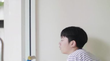 Çocuk bir gülümseme yüz ile evi silmek için cam bir bez kullanıyor, Evde genç asya çocuk temizlik aynası.