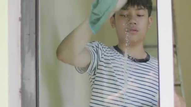 少年は笑顔で家を拭くためにガラスの布を使用しています 自宅で鏡を掃除する若いアジアの少年 — ストック動画