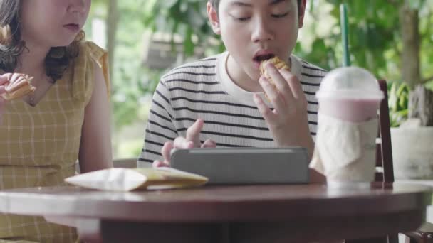 妹とアジアの男の子は笑顔でタブレットコンピュータで遊んで食べるのを楽しむ — ストック動画