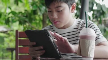 Asyalı çocuk gülümseme yüzü ile tablet bilgisayarda oynuyor.