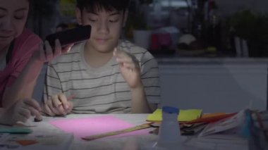 Şiddetli yağmurun yağdığı gün elektrikler kesildi, Asyalı anneler işi bitirmek için telefon lambasını kullanarak oğluma sanat yapmasında yardım ettiler..