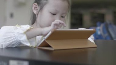 Küçük Asyalı kız kütüphanede annesiyle dijital tablette oynuyor.