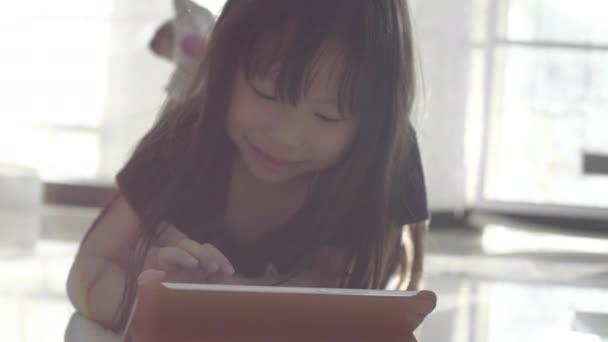 幸せな小さなアジアの女の子見ますオンタブレットコンピュータとアクション飛行上の空気 — ストック動画