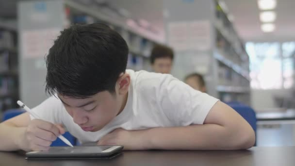 亚洲青少年在图书馆使用平板电脑 两个男孩笑着在平板电脑上画画 — 图库视频影像