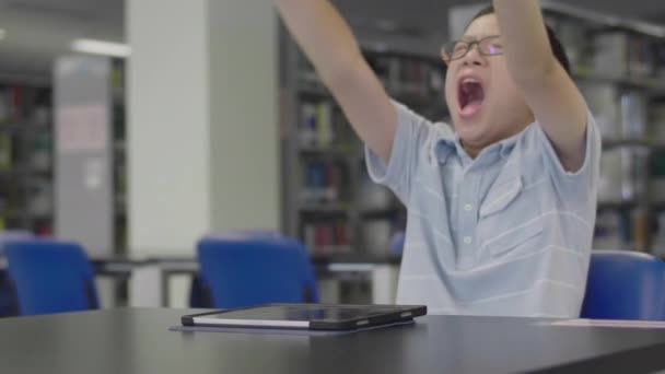 Vicces Iskolás Fiú Egy Íróasztalnál Könyvtárban Unatkozik Ásít — Stock videók
