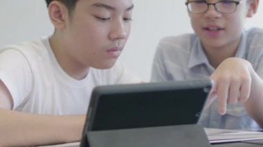 Asyalı ergenler kütüphanede tablet bilgisayar kullanıyorlar. Tablet bilgisayarına gülen yüzlü iki çocuk çiziyor..