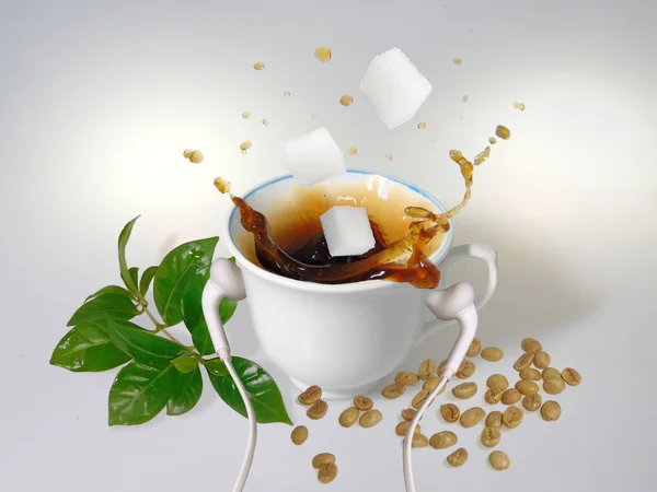 A white cup with white earphones put on it, splash of coffee, three  sugar cubes, green coffee beans and leaves