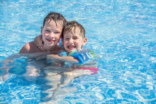 Older brother and younger brother swim in the outdoor children\'s pool