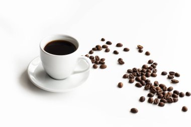 Beyaz kahve fincanı ve çay tabağı beyaz bir masaya serpiştirilmiş kahve taneleri.