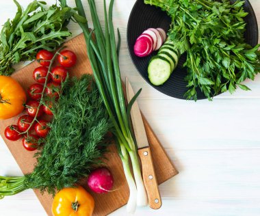 Hafif arka planda vejetaryen yemekleri, kesme tahtasında taze sebzeler ve metin için yeri olan tabakta yeşiller.