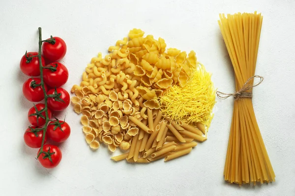 Different types of pasta shells long noodles and raw spaghetti and cherry tomatoes top view