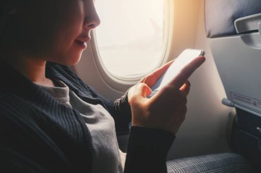 Turist Asyalı kadın uçak penceresi yakınında oturan ve Smart kullanarak