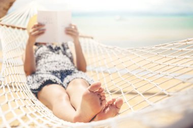 Woman reading a book on hammock beach in free time summer holida clipart