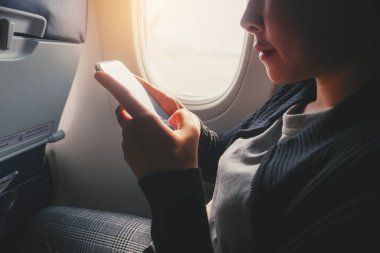 Turist Asyalı kadın uçak penceresi yakınında oturan ve Smart kullanarak