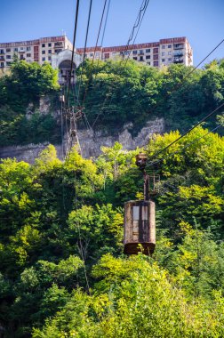 Yukarıda mavi gökyüzü ve binalar ile alt istasyondan halatlar asılı eski bir teleferik görünümü.