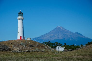 Arka planda Dağ Taranaki ve yukarıda mavi gökyüzü ile Cape Egmont Deniz Feneri. Egmont Ulusal Parkı, Yeni Zelanda Kuzey Adası