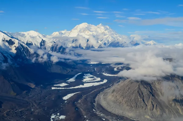 Aerial view of Alaska mountaion range around Denali peak from a plane with glaciers around and blue sky above. Denali National Park