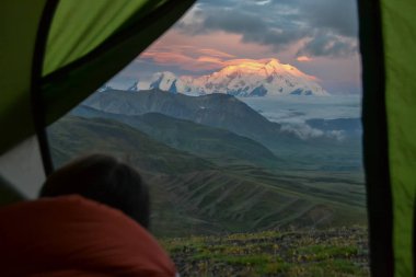 Kişi Denali Dağı'nın gündoğumu görünümünde bir çadırdan bakıyor - Stony Dome bakan kırmızı alpenglow ile mt Mckinley zirvesi. Denali Ulusal Parkı