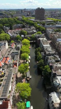 Çarpıcı hava görüntüleri, canlı kentsel bir çevre içinde kurulmuş yemyeşil ve büyüleyici tarihi binalarla çevrili Amsterdam kanalını güzel bir şekilde gösteriyor.