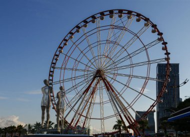 Batum,Acara,Gürcistan - 06 Temmuz 2019, Batum seti, batan güneşin ışınlarında dönme dolap, aşk heykelinin arka planında