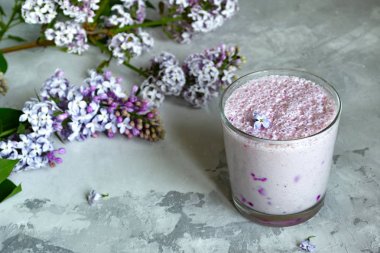 Bardakta berry milkshake. Leylak çiçekleri ile dekore edilmiş gri bir arka plan üzerinde yaban mersini ile yaz kokteyli. Provence tarzı