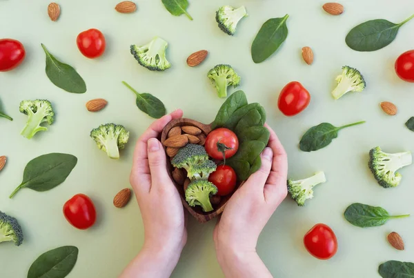 緑の背景に心のための健康食品 女性の手は野菜とプレートを保持 ほうれん草とナッツ スーパーフードと健康の概念 トップビュー フラットレイアウト — ストック写真