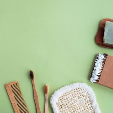 Çevre dostu ürünler yeşil arka planda. Bambu diş fırçaları, pamuk tomurcukları, tarak, doğal sabun ve bez. Üst görünüm, düz görünüm, kopyalama alanı