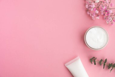 Açık pembe arka planda kozmetik ürünleri ve çiçekler. Doğal kozmetik, güzellik, cilt bakımı. Üst görünüm, düz görünüm, kopyalama alanı