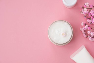 Açık pembe arka planda kozmetik ürünleri ve çiçekler. Doğal kozmetik, güzellik, cilt bakımı. Üst görünüm, düz görünüm, kopyalama alanı