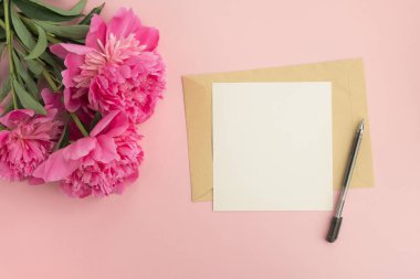 Pembe şakayık çiçekleri ve pastel arka planda boş bir kartın olduğu bir zarf. Üst görünüm, düz görünüm, kopyalama alanı