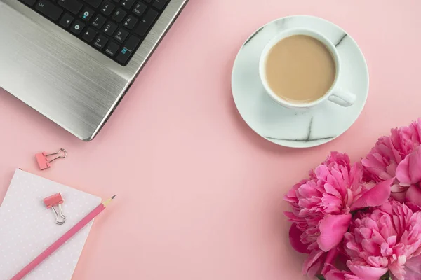 Office pink table. Workplace with laptop, notepad, peony flowers and coffee. Top view, flat lay, copy space