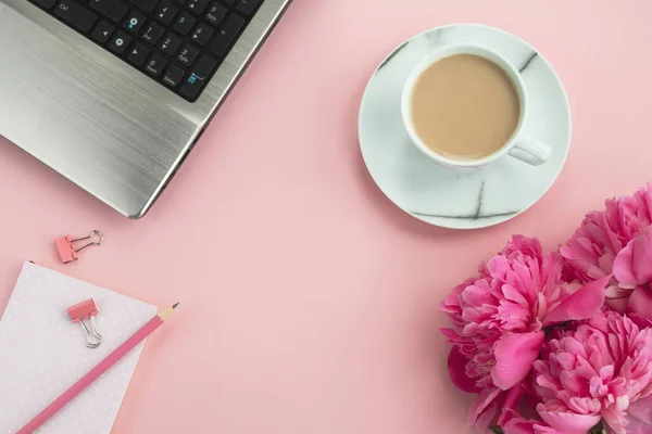 Ofis pembe masası. Dizüstü bilgisayarı, not defteri, şakayık çiçekleri ve kahvesi olan bir iş yeri. Üst görünüm, düz görünüm, kopyalama alanı