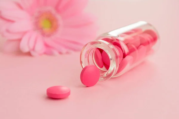 Women\'s health, medicine and healthcare concept. Pink pills and glass bottle on flower background. Close up