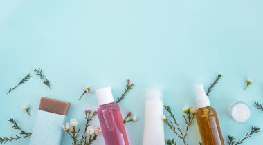 Doğal kozmetik. Kozmetik ürünleri olan çeşitli şişeler ve pastel arka planda çiçekler. Güzellik, cilt bakımı konsepti. Üst görünüm, düz görünüm, kopyalama alanı