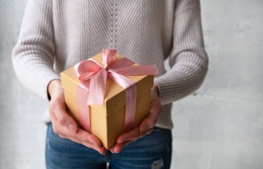 Kadının elinde pembe kurdeleli hediye paketi var. Tatil, hediyeler ve indirim konsepti. Kapat, boşluğu kopyala