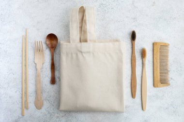 Plastiksiz mutfak ve banyo aksesuarları. Tekstil eco çantası, ahşap çatal bıçak takımı, tarak ve bambu diş fırçaları beyaz masada. Sıfır israf yaşam tarzı. Üst manzara, düz uzanma