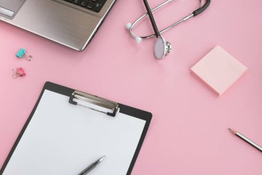 Tıbbi steteskobu, bilgisayarı ve pembe masasında boş bir panosu olan bir doktor. Sağlık ve tıp konsepti. Boşluğu kopyala