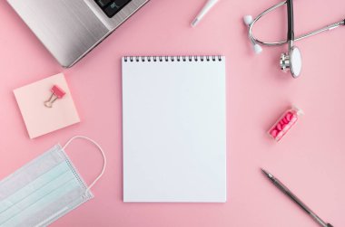 Doktor işyeri ve tıbbi ekipmanlar pembe arka planda. Boş not defteri, steteskop, laptop, koruyucu yüz maskesi, termometre, haplar ve kalem. Üst görünüm, düz görünüm, kopyalama alanı