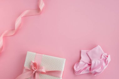 Bir çift küçük bebek çorabı ve pembe arka planda hediye kutusu. Yeni doğmuş kız aksesuarları. Kartpostal, davetiye, bebek partisi. Üst görünüm, düz görünüm, kopyalama alanı