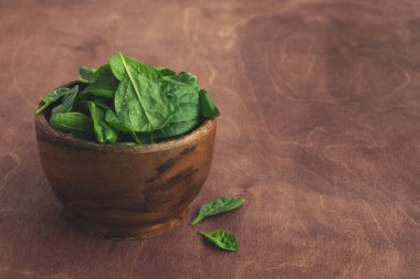 Mutfak masasındaki ahşap bir kasede ıspanak yaprakları. Sağlıklı yemek, vejetaryen diyet konsepti. Boşluğu kopyala, kapat