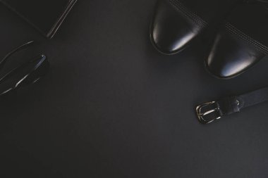 Siyah arka planda moda adamı aksesuarları. Ayakkabılar, deri kemer, cüzdan ve güneş gözlüğü. Üst görünüm, düz görünüm, kopyalama alanı